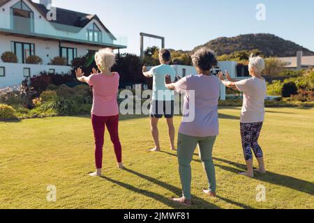 Multirassische Senioren, die sich die Hände strecken, während sie auf grasbewachsenem Land im Hof des Pflegeheims stehen Stockfoto