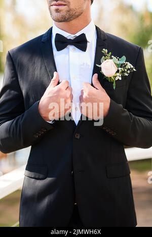 Hes bindet den Knoten mit Stil. Ein unkenntlich junger Bräutigam passt seinen Anzug an und bereitet sich an seinem Hochzeitstag draußen vor. Stockfoto