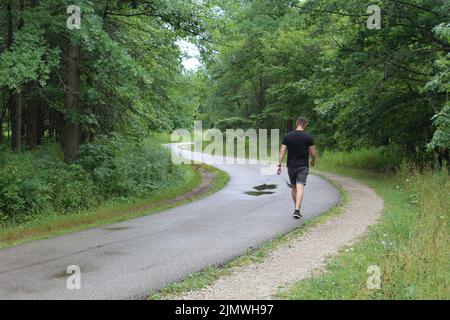 Mann in schwarzer Kleidung, der an einem regnerischen Tag auf dem North Branch Trail in den Bunker Hill Woods in Chicago spazierengeht Stockfoto