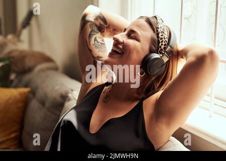 Musik ist der Weg zu meinem Herzen. Eine junge Frau, die zu Hause Kopfhörer auf dem Sofa benutzt. Stockfoto