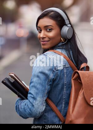 Eine junge Frau, die mit Kopfhörern durch die Stadt läuft und dabei ihre Bücher trägt. Stockfoto