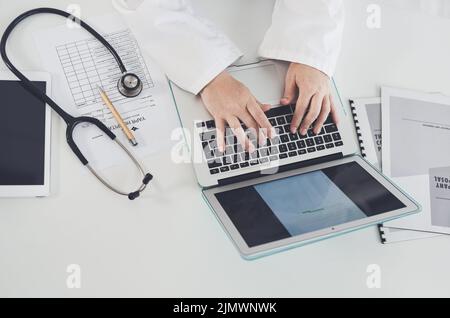 Die drahtlose Technologie hat sich zum Zentrum der Ärzte entwickelt. High-Angle-Aufnahme einer nicht erkennbaren Ärztin, die während der Arbeit in ihrem Büro einen Laptop verwendet. Stockfoto