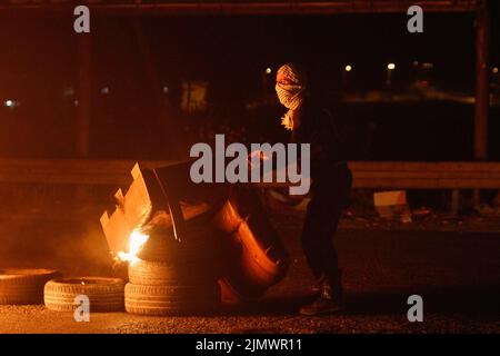 Nablus, Palästina. 07. August 2022. Ein palästinensischer Demonstranten verbrennt Reifen, um die Hauptstraße in der Nähe des von Israel kontrollierten Hawara-Kontrollpunkts südlich von Nablus zu blockieren, während der Proteste gegen die israelischen Luftangriffe auf Gaza, bei denen mindestens 41 Palästinenser getötet wurden. (Foto von Nasser Ishtayeh/SOPA Images/Sipa USA) Quelle: SIPA USA/Alamy Live News Stockfoto