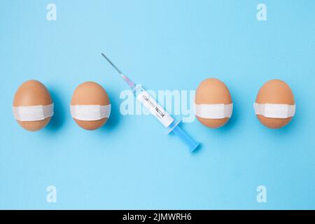 Flatlay mit Monkeypox-Impfstoffspritze und geimpften Eiern mit medizinischem Pflaster auf blauem Hintergrund. Stockfoto