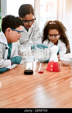 Und so entsteht Dampf... ein entzückendes kleines Mädchen und Junge, die mit ihrem Lehrer in der Schule ein wissenschaftliches Experiment durchführen. Stockfoto