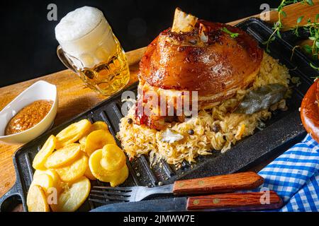 Rustikales Schweinshaxe mit Sauerkraut, süßem Senf und gebratenen Kartoffeln Stockfoto