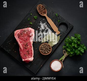 Frisches rohes Stück Rindfleisch, Striploin-Steak auf schwarzem Hintergrund, Draufsicht. Marmoriertes Stück Fleisch Stockfoto