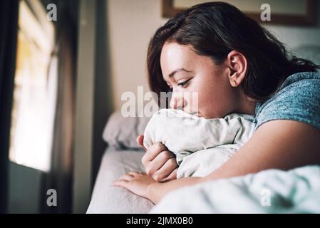 Sie erwachte mit einem gebrochenen Herzen. Eine attraktive junge Frau, die deprimiert aussblickte, als sie zu Hause auf ihrem Bett lag. Stockfoto