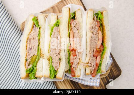 Flach auf gewickelt Thunfisch Sandwich mit Salat Tomaten, Gurken und Zwiebeln in Weidenkorb halbiert Stockfoto