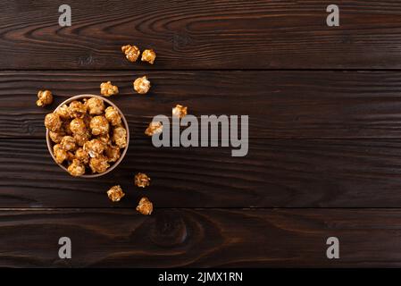 Karamellisiertes Popcorn in Papiereimer auf hölzernen Küchentisch flach legen Stockfoto