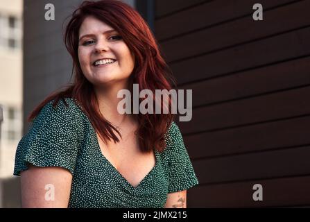 Rote Haare geben mir mehr Selbstvertrauen. Eine schöne junge Frau posiert im Freien. Stockfoto