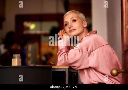 Die Dinge schauen endlich nach mir. Eine attraktive junge Frau, die nachdenklich aussieht, während sie sich in einem Café entspannt. Stockfoto