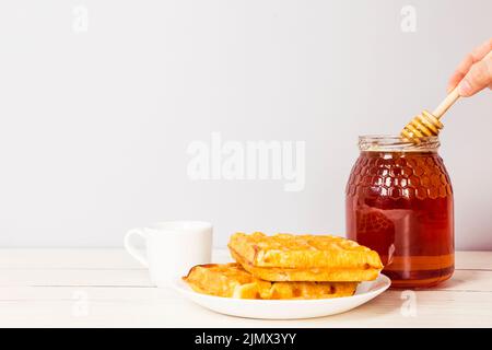 Hand hält Honig Dipper aus Glas Honig leckeren Frühstückstisch Stockfoto