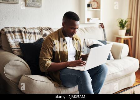 Zeit für die Arbeit an seinem Blog. Ein hübscher junger Mann, der einen Laptop benutzt, während er sich zu Hause auf seiner Couch entspannt. Stockfoto
