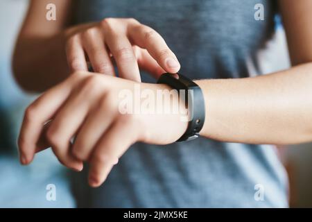 Ich muss überprüfen, wie viele Kalorien ich verbrenne. Eine unkennbare Frau, die allein in ihrem Haus steht und ihren Fitness-Tracker vor dem Training einsetzt. Stockfoto