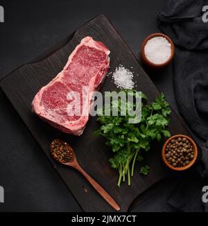 Frisches rohes Stück Rindfleisch, Striploin-Steak auf schwarzem Hintergrund, Draufsicht. Marmoriertes Stück Fleisch Stockfoto