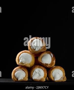 Gebackene Tubuli gefüllt mit geschlagener Eiweiß-Creme auf einem schwarzen Küchenbrett aus Holz Stockfoto