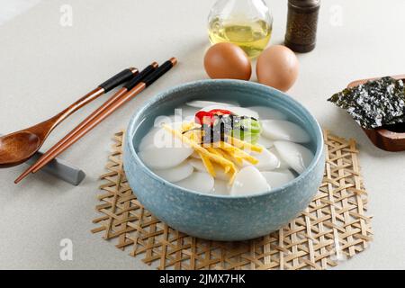 Koreanische Tortengruppe oder Tteokguk auf blauer Schale. Belag mit Ei, Chili, Algen und Frühlingszwiebeln. Beliebte Suppe für Familientreffen Stockfoto