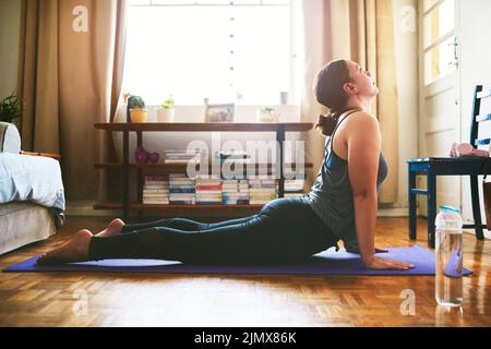 Öffnen der Brust. Eine attraktive junge Frau sitzt und hält eine Kobra-Pose, während sie Yoga in ihrem Haus macht. Stockfoto