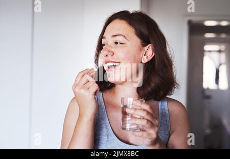 Tun Sie, was es braucht, um eine gute Gesundheit zu erhalten. Eine junge Frau, die Medikamente zu Hause nimmt. Stockfoto