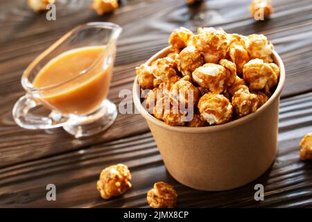 Karamellisiertes Popcorn in Papiereimer auf Holztisch Stockfoto