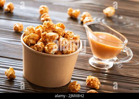 Karamellisiertes Popcorn in Papiereimer auf Holztisch Stockfoto