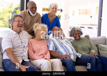 Fröhliche multirassische männliche und weibliche ältere Freunde, die lachen, während sie sich im Pflegeheim entspannen Stockfoto