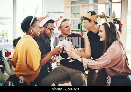 Jubel zu der schönsten Zeit des Jahres. Eine Gruppe von fröhlichen jungen Freunden, die anstoßen, während sie Weihnachten gemeinsam zu Hause feiern. Stockfoto