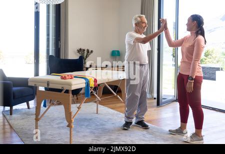 Glücklicher kaukasischer älterer Mann, der zu Hause eine Birazialphysiotherapeutin mit einem hohen Fünftel übergab, Platz zum Kopieren Stockfoto