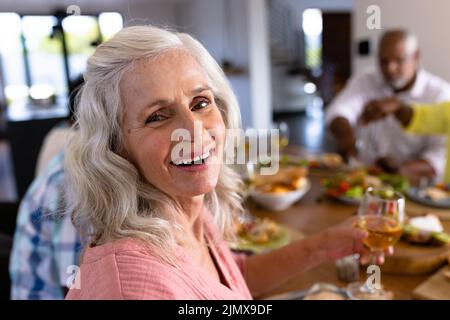 Porträt einer älteren Frau aus mehreren Rassen, die beim Mittagessen mit Freunden am Esstisch Wein genießt Stockfoto