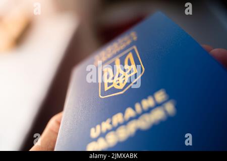 Ukrainischer biometrischer Pass in der Hand, Nahaufnahme vor verschwommenem Hintergrund. Wappen der Ukraine in Form eines Dreizacks. Blaues Dokument Nachweis der Identifikation Stockfoto