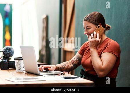 Lassen Sie mich das für Sie überprüfen: Eine attraktive junge Geschäftsfrau, die allein sitzt und ihr Handy benutzt, während sie ihren Laptop benutzt. Stockfoto
