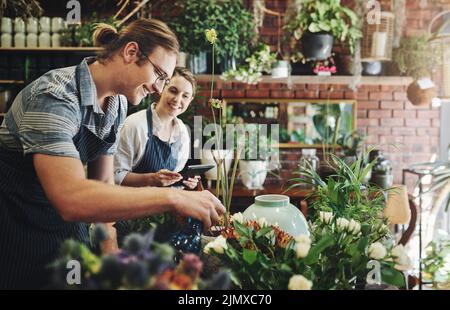 Sie lernen jeden Tag etwas Neues, wenn Sie mit Pflanzen arbeiten. Zwei junge Floristen gießen Blumen und arbeiten zusammen in ihrer Pflanzenkinderstube. Stockfoto