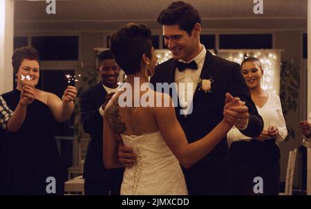 Habe ich erwähnt, wie schön Sie sind. Ein liebevolles junges frisch verheiratetes Paar tanzt, während ihre Gäste Sparkler bei ihrer Hochzeit halten Stockfoto