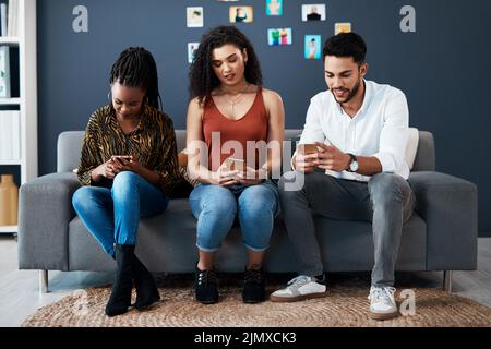 Und das alles in ihrer eigenen digitalen Welt. In voller Länge eine Gruppe von Geschäftskollegen, die zusammen auf einem Sofa sitzen und ihre Mobiltelefone benutzen. Stockfoto