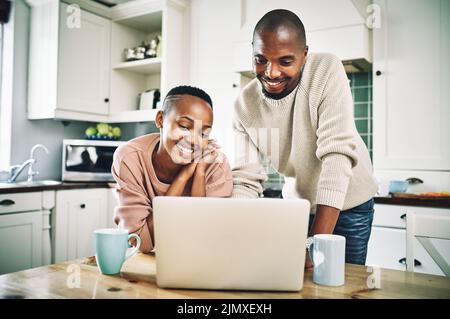 Ein glückliches junges Paar, das einen Laptop benutzt, während es sich zu Hause entspannt. Stockfoto