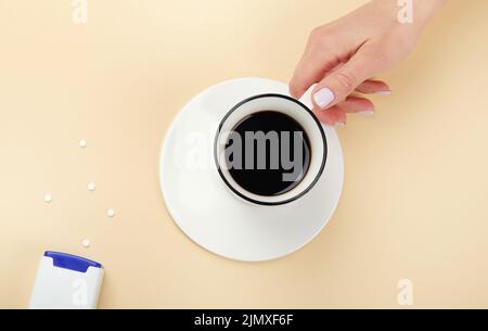 Nahaufnahme einer Frau, die auf weißem Hintergrund Saccharin-Pillen in eine Kaffeetasse wirft, Draufsicht. Stockfoto