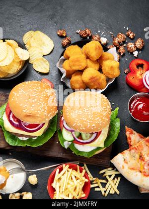 Fast Food und ungesunde Ernährung Konzept - Nahaufnahme von Fast-Food-Snacks und Cola-Getränken auf dunklem Hintergrund, Draufsicht. Stockfoto
