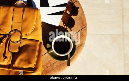 Es ist immer Kaffeezeit. Eine Tasse Kaffee und eine Tüte, die tagsüber auf einem Couchtisch aufgelegt wurde, wurden in einem hohen Winkel aufgenommen. Stockfoto