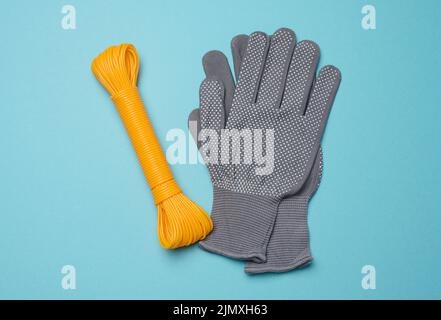 Ein Paar graue textile Arbeitshandschuhe und ein orangefarbenes Seil auf blauem Hintergrund, Draufsicht Stockfoto