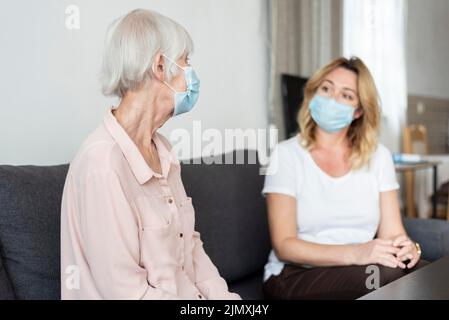 Frau, die ihr relatives Pflegeheim in einer medizinischen Maske besucht Stockfoto