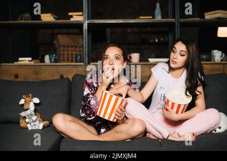 Frau beim Film, während ihre Freundin Popcorn aus ihrem Eimer nimmt Stockfoto