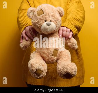 Frau in orange gestrickt Pullover Umarmungen niedlichen braunen Teddybär. Stockfoto