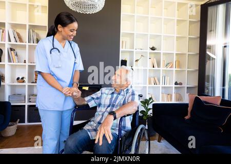 Biraziale Gesundheitshelferin, die einen kaukasischen älteren Mann unterstützt, der auf dem Rollstuhl sitzt Stockfoto