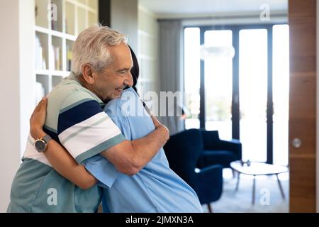 Kaukasischer älterer Mann und biraziale weibliche Gesundheitshelferin umarmen sich zu Hause Stockfoto