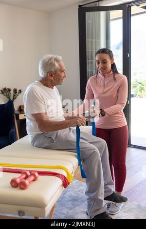 Biracial weibliche Physiotherapeutin hilft älteren Mann mit Resistenzbändern trainieren Stockfoto