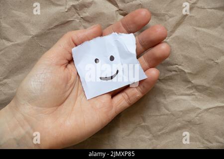 Ein fröhliches Emoticon wird in den Händen einer Frau auf ein Blatt Papier gezeichnet, gute Laune, Freude und ein Lächeln Stockfoto