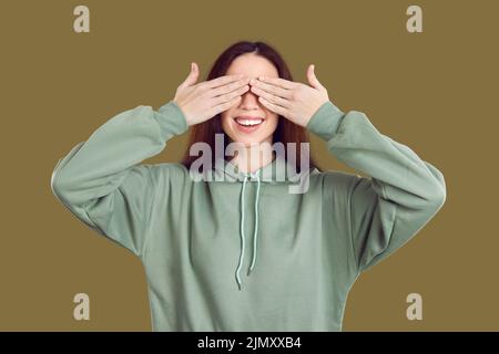 Lustige lächelnde Frau in Erwartung von etwas Interessantes schließt ihre Augen mit ihren Händen. Stockfoto