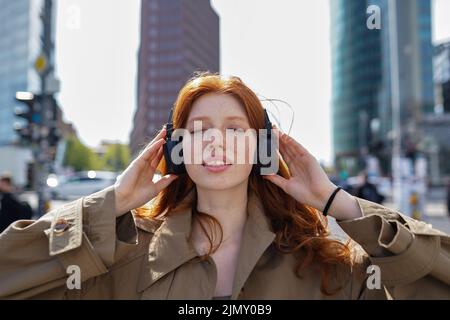 Happy teen rothaarige Mädchen trägt Kopfhörer Musik hören in der Großstadt. Stockfoto