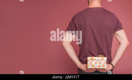 Rückansicht Mann versteckt florale Geschenkbox vor farbigem Hintergrund Stockfoto